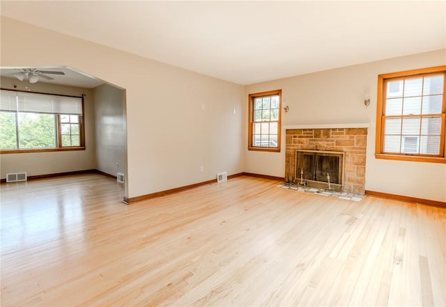 unfurnished living room featuring ceiling fan, light hardwood / wood-style floors, a stone fireplace, and a wealth of natural light