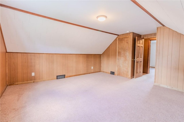 additional living space with light carpet, wooden walls, and vaulted ceiling