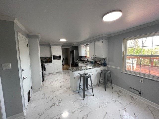 kitchen featuring appliances with stainless steel finishes, kitchen peninsula, white cabinetry, and ornamental molding