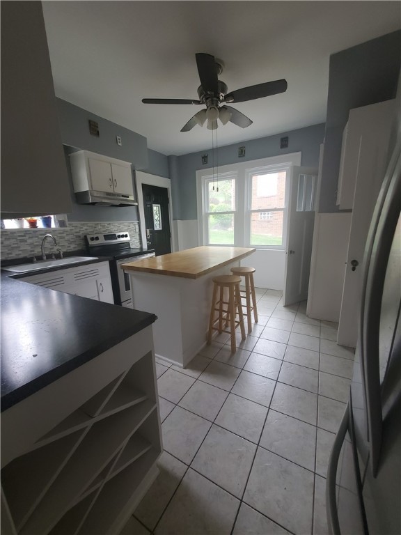 kitchen with a breakfast bar, sink, a center island, electric range, and decorative backsplash