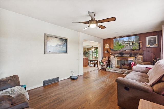 living room featuring wood-type flooring, a stone fireplace, and ceiling fan