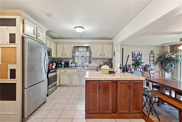 kitchen with tile countertops, cream cabinets, light tile patterned floors, and stainless steel appliances