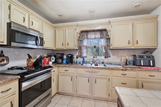 kitchen with appliances with stainless steel finishes, backsplash, light tile patterned floors, cream cabinets, and tile countertops