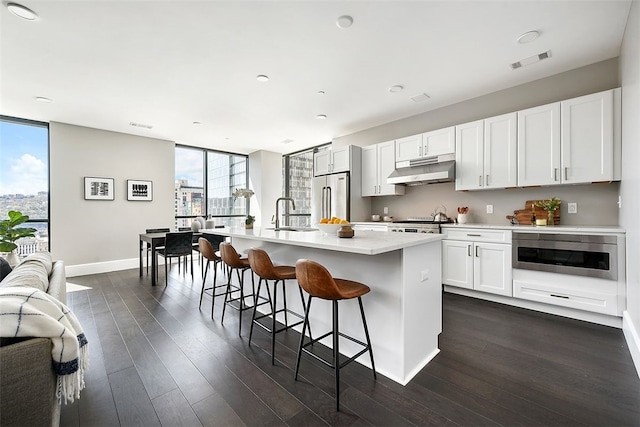 kitchen featuring a healthy amount of sunlight, floor to ceiling windows, an island with sink, and high end refrigerator