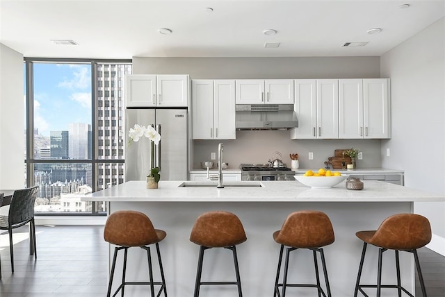 kitchen with sink, dark wood-type flooring, stove, high end fridge, and an island with sink