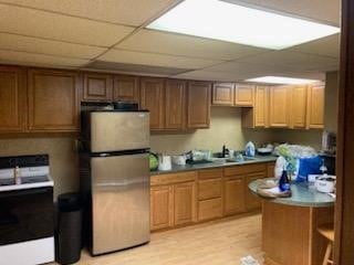 kitchen featuring electric range oven, light hardwood / wood-style floors, a drop ceiling, and stainless steel refrigerator