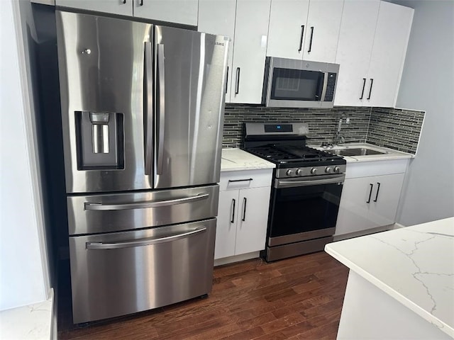 kitchen with light stone counters, appliances with stainless steel finishes, sink, backsplash, and dark wood-type flooring