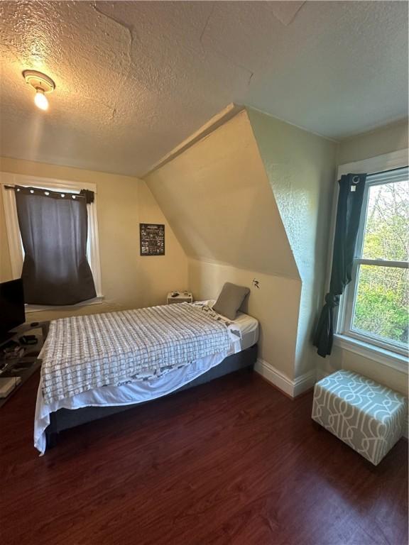 bedroom featuring vaulted ceiling, dark hardwood / wood-style flooring, and a textured ceiling