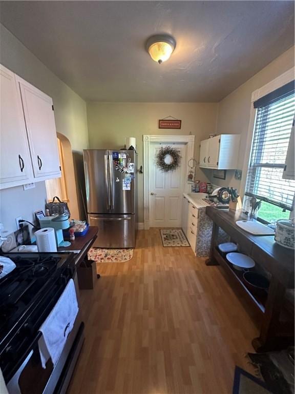 kitchen with white cabinets, black range, stainless steel fridge, and light hardwood / wood-style flooring