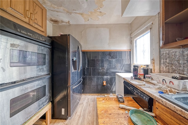 kitchen featuring tile walls, light hardwood / wood-style floors, black fridge, and double wall oven