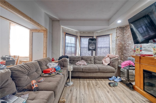 living room with a fireplace, light hardwood / wood-style floors, and brick wall