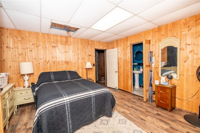 bedroom featuring a drop ceiling, a sink, wooden walls, and wood finished floors