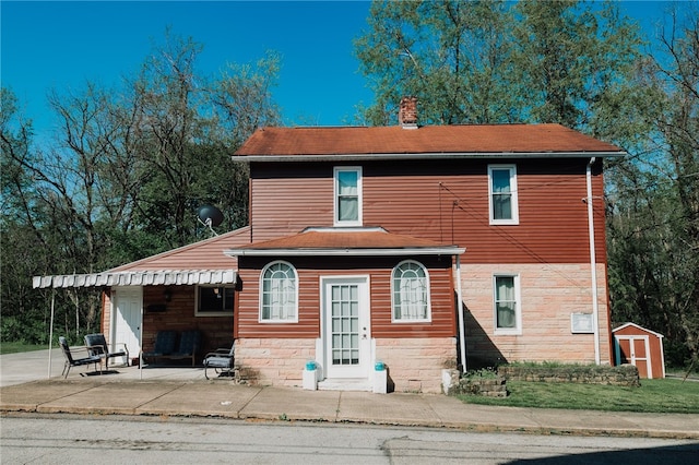 back of property featuring a storage shed, a chimney, and an outdoor structure