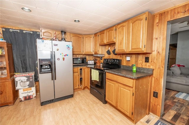 kitchen featuring light wood-type flooring, appliances with stainless steel finishes, wood walls, and dark countertops