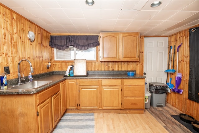 kitchen with light wood-style flooring, dark countertops, a sink, and wooden walls