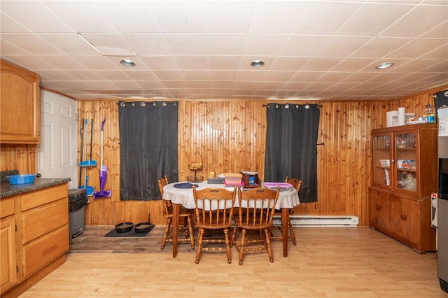 dining area with light wood-style floors, a baseboard radiator, and wooden walls