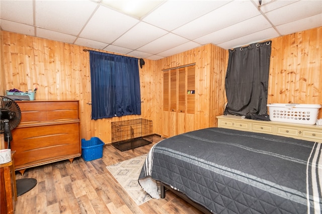 bedroom featuring a paneled ceiling, a closet, wooden walls, and wood finished floors