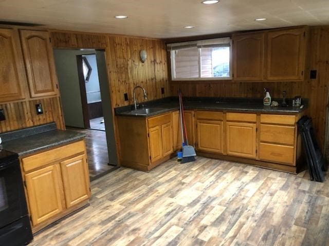 kitchen with dark countertops, electric range, light wood-style flooring, a sink, and wooden walls