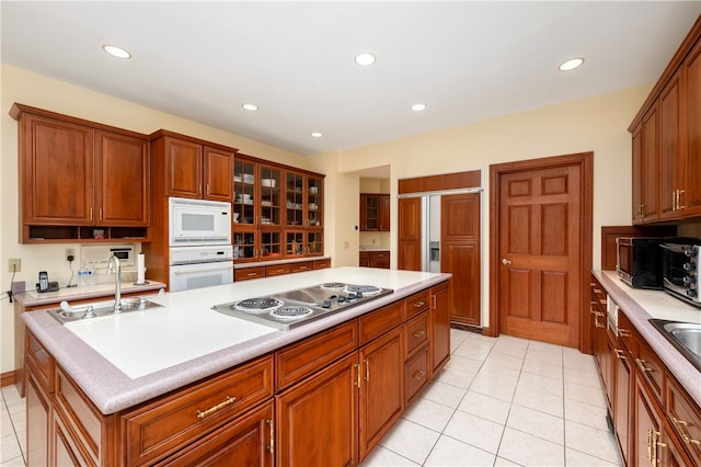 kitchen featuring an island with sink, sink, light tile flooring, and white appliances