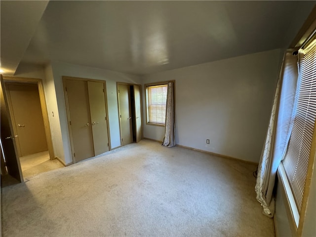 unfurnished bedroom featuring light carpet and multiple closets