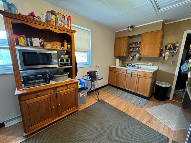 kitchen with light wood-type flooring, crown molding, baseboard heating, and sink