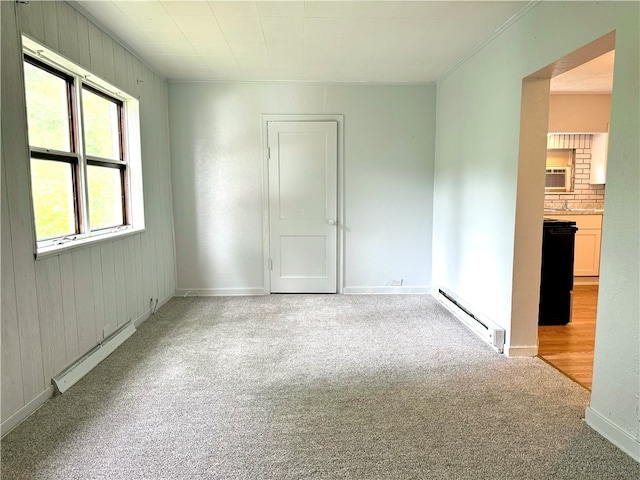 empty room featuring a baseboard radiator, wooden walls, and light colored carpet