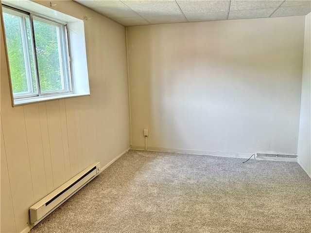 carpeted empty room featuring a baseboard heating unit and a paneled ceiling