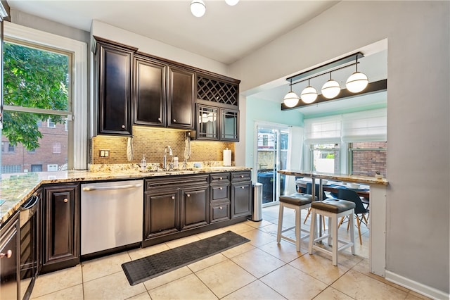 kitchen with decorative light fixtures, backsplash, sink, light stone counters, and dishwasher