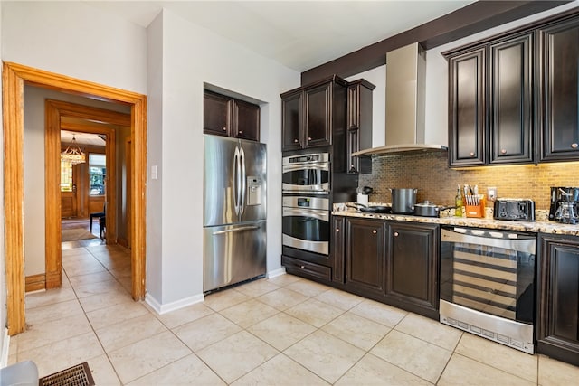 kitchen featuring light stone countertops, appliances with stainless steel finishes, backsplash, wall chimney range hood, and light tile floors