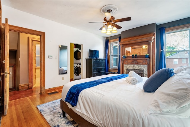 bedroom featuring stacked washer and clothes dryer, ceiling fan, a tile fireplace, and hardwood / wood-style flooring