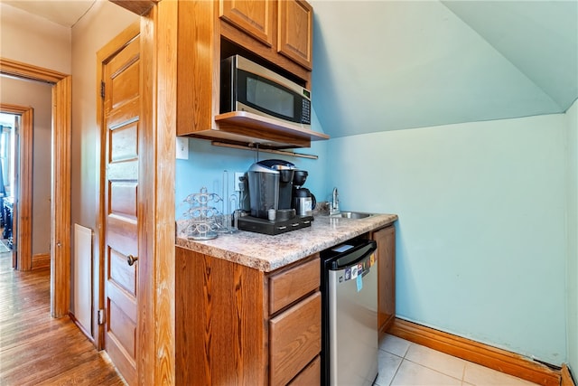 kitchen featuring sink, stainless steel appliances, light tile floors, and lofted ceiling