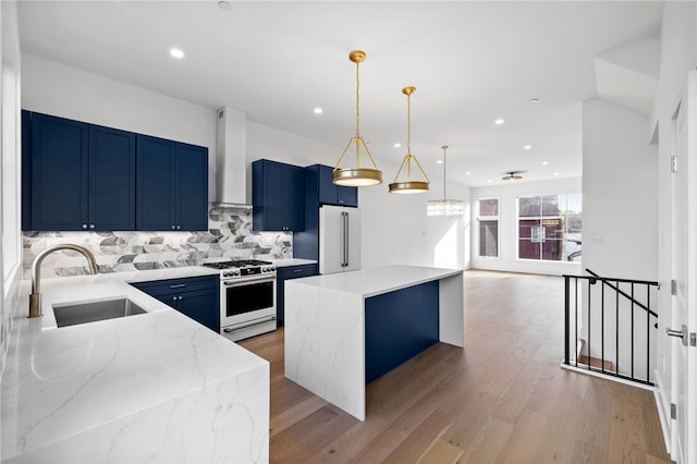 kitchen with wall chimney exhaust hood, sink, stainless steel range with gas cooktop, high end white fridge, and hardwood / wood-style floors