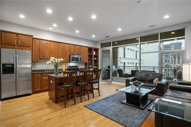 interior space featuring appliances with stainless steel finishes, a kitchen island, sink, light wood-type flooring, and a breakfast bar