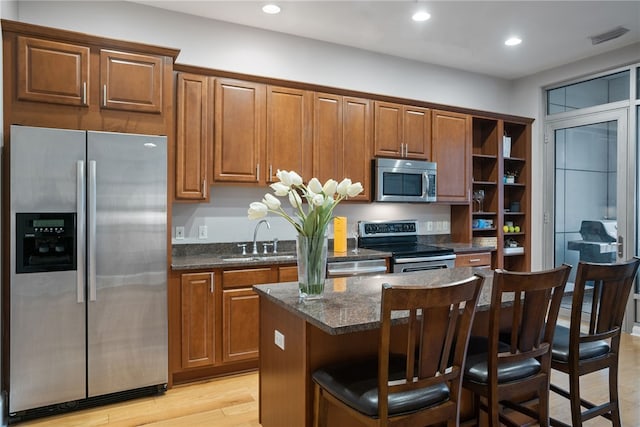 kitchen with appliances with stainless steel finishes, a kitchen island, light hardwood / wood-style floors, dark stone counters, and sink