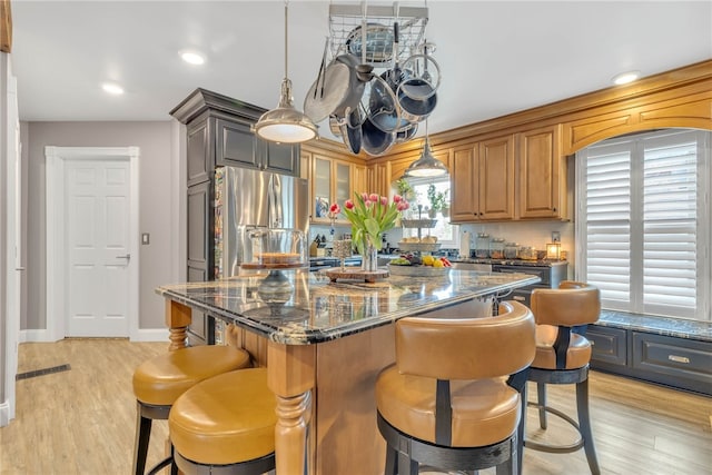 kitchen featuring decorative light fixtures, light hardwood / wood-style flooring, dark stone counters, stainless steel fridge, and a center island