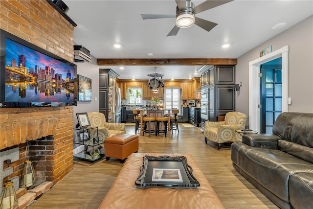 living room featuring light hardwood / wood-style floors, ceiling fan, a fireplace, and beam ceiling