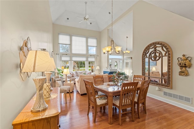 dining space featuring ceiling fan with notable chandelier, hardwood / wood-style floors, and high vaulted ceiling