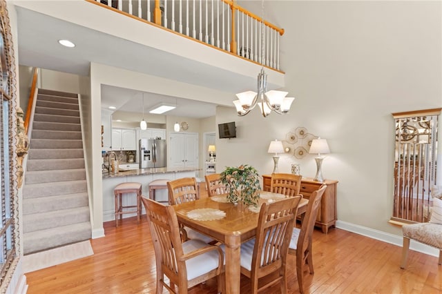 dining space with an inviting chandelier, light hardwood / wood-style floors, and a high ceiling