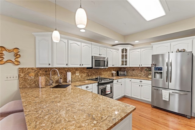 kitchen with white cabinetry, pendant lighting, stainless steel appliances, light hardwood / wood-style flooring, and sink