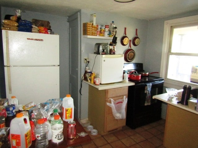 kitchen featuring white refrigerator, black / electric stove, and tile floors