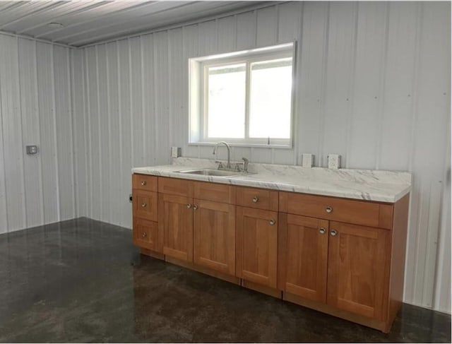 kitchen featuring concrete flooring, light stone counters, a sink, and brown cabinets