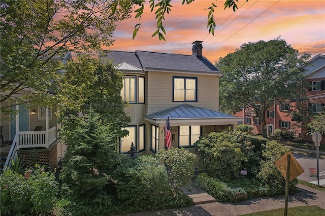 view of front of home with a standing seam roof, metal roof, a chimney, and roof with shingles