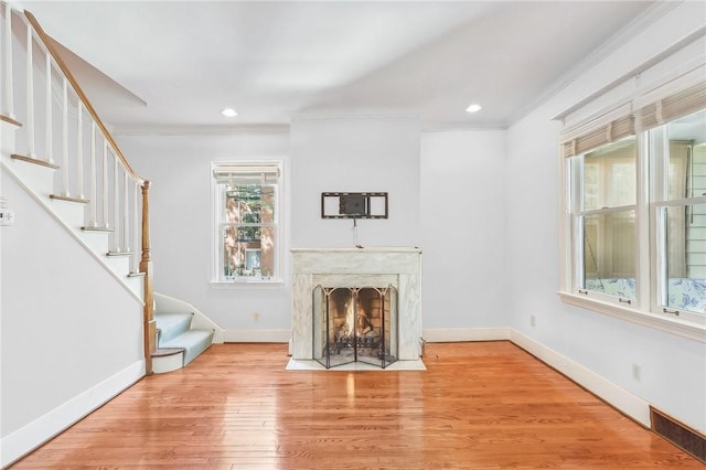 unfurnished living room featuring baseboards, a premium fireplace, wood finished floors, stairs, and crown molding