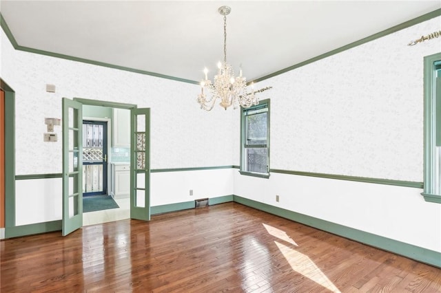 unfurnished room featuring hardwood / wood-style flooring, a notable chandelier, ornamental molding, and wallpapered walls