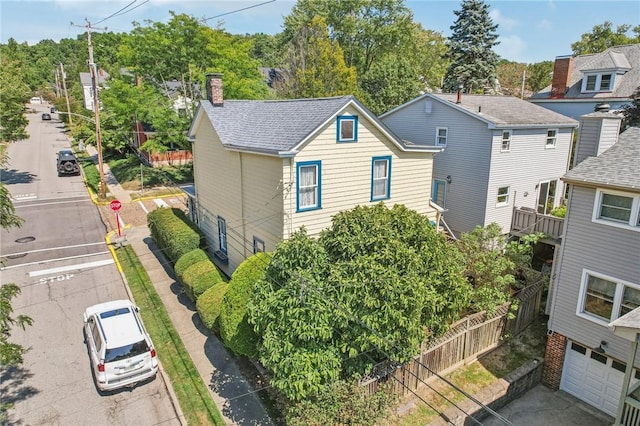 exterior space with roof with shingles, a chimney, fence, a garage, and driveway