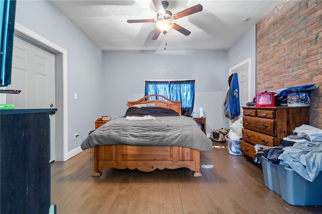 bedroom featuring brick wall, wood-type flooring, and ceiling fan