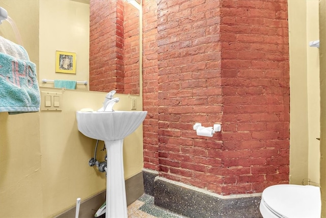 bathroom featuring brick wall and toilet