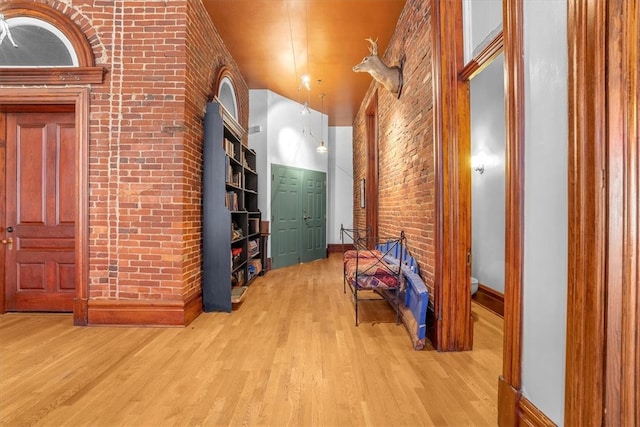 hall with brick wall, light hardwood / wood-style floors, and ornamental molding