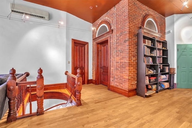 hall with a wall mounted air conditioner, vaulted ceiling, and light wood-type flooring