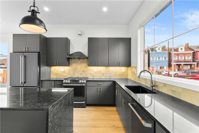 kitchen featuring appliances with stainless steel finishes, sink, hanging light fixtures, light hardwood / wood-style floors, and wall chimney range hood